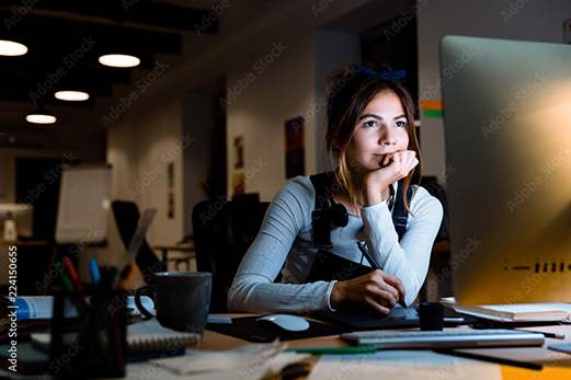 Designer working late at desk, screen light, candid and absorbed