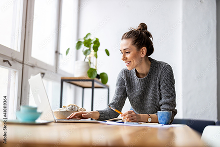 Woman smiling at laptop in bright home workspace